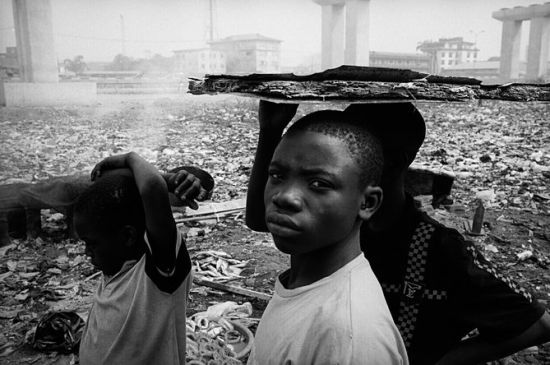 尼日利亚拉各斯市，Orile-Iganmu的Doyin垃圾场。拾荒者从卡车上搬运电子垃圾并倾倒入垃圾场。这里的孩子们纷纷跑来并把他们能找到的任何东西撕碎，希望能从中找到一些金属，尤其是铜和金。